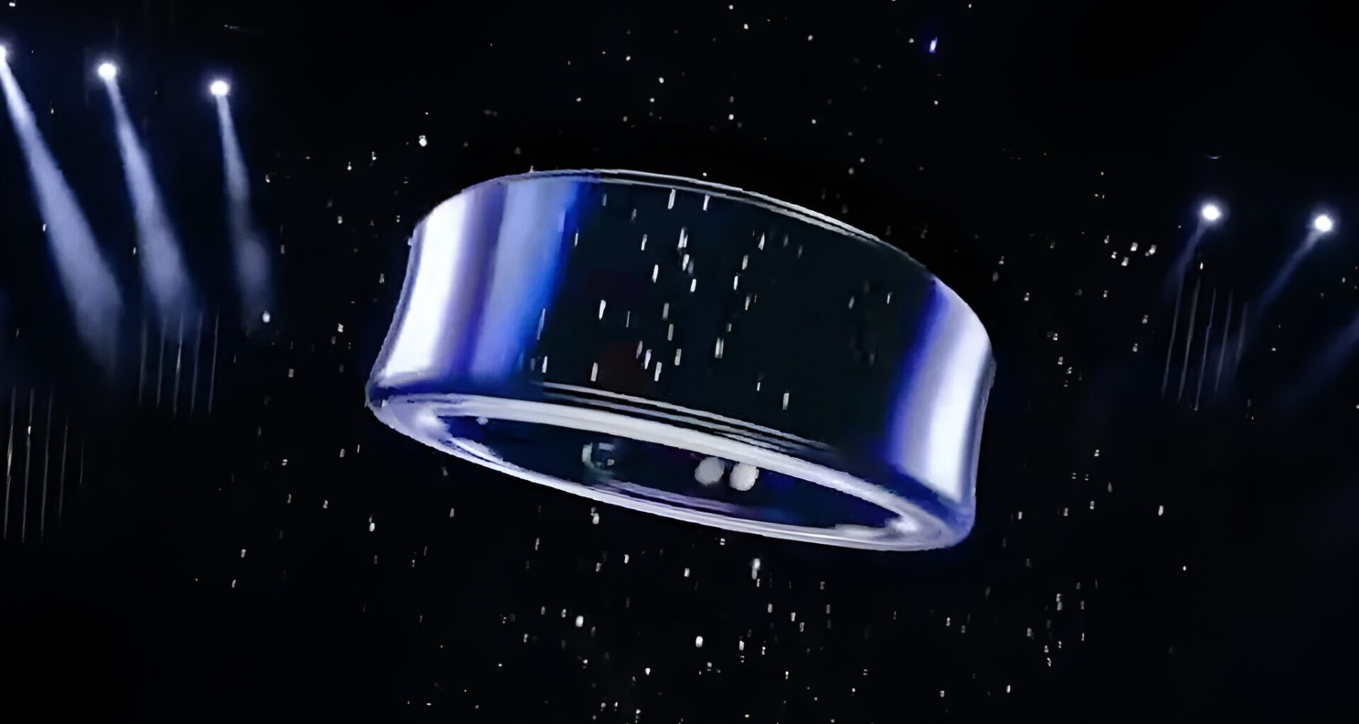 A metallic ring-shaped object is suspended in a dark space with spotlight illumination and a starry background.