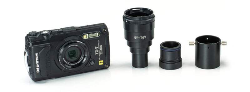 A black OM SYSTEM TG-7 camera is shown on the left, placed next to three detachable black camera lens adapters and accessories arranged in a row on a white background.