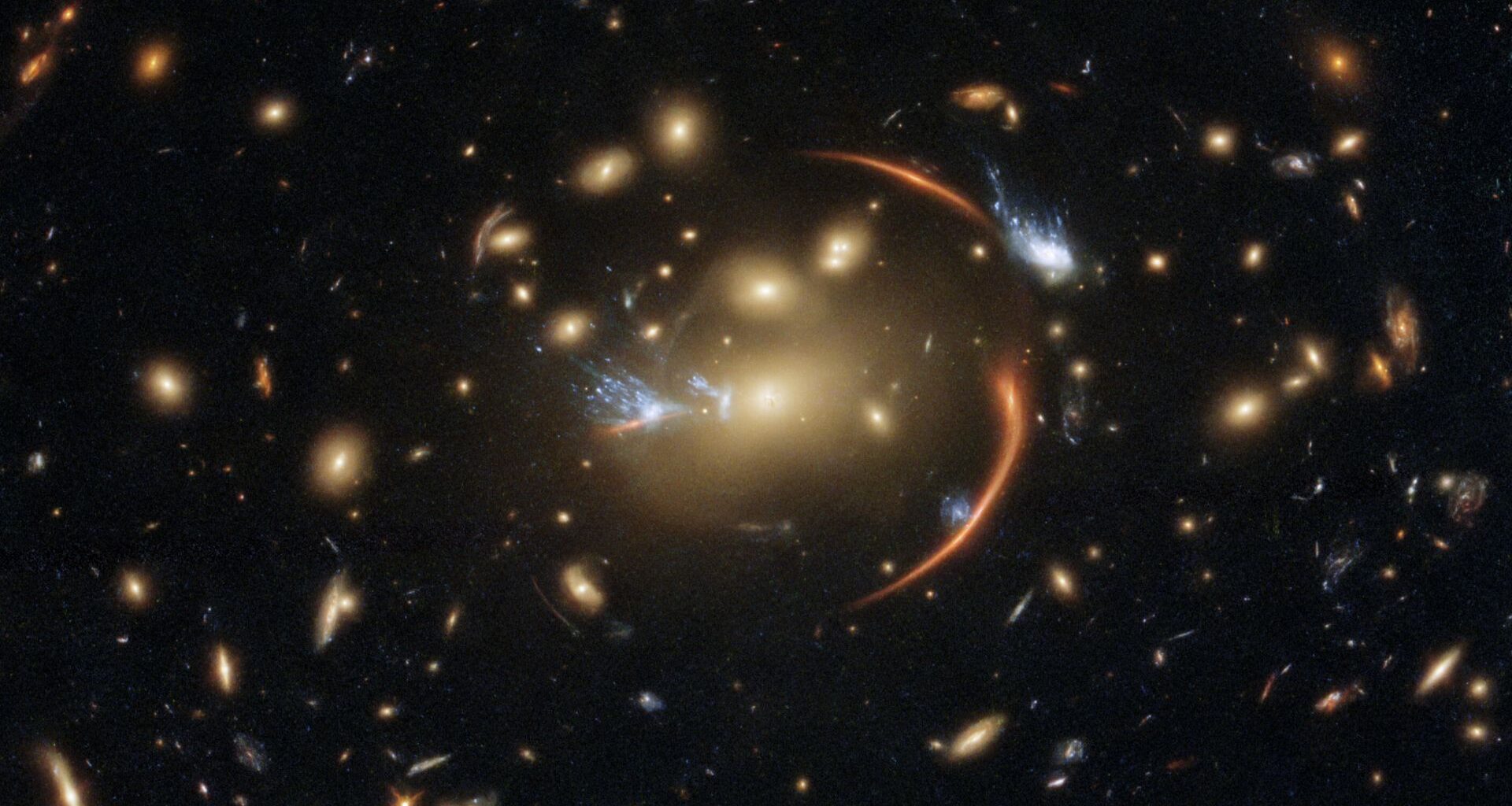 A deep space image shows the phenomenon of gravitational lensing, with a circular ring of light bubbled around a golden star in the center of the image. The rest of the image seems bulged into a fish-eye circular shape due to the lensing
