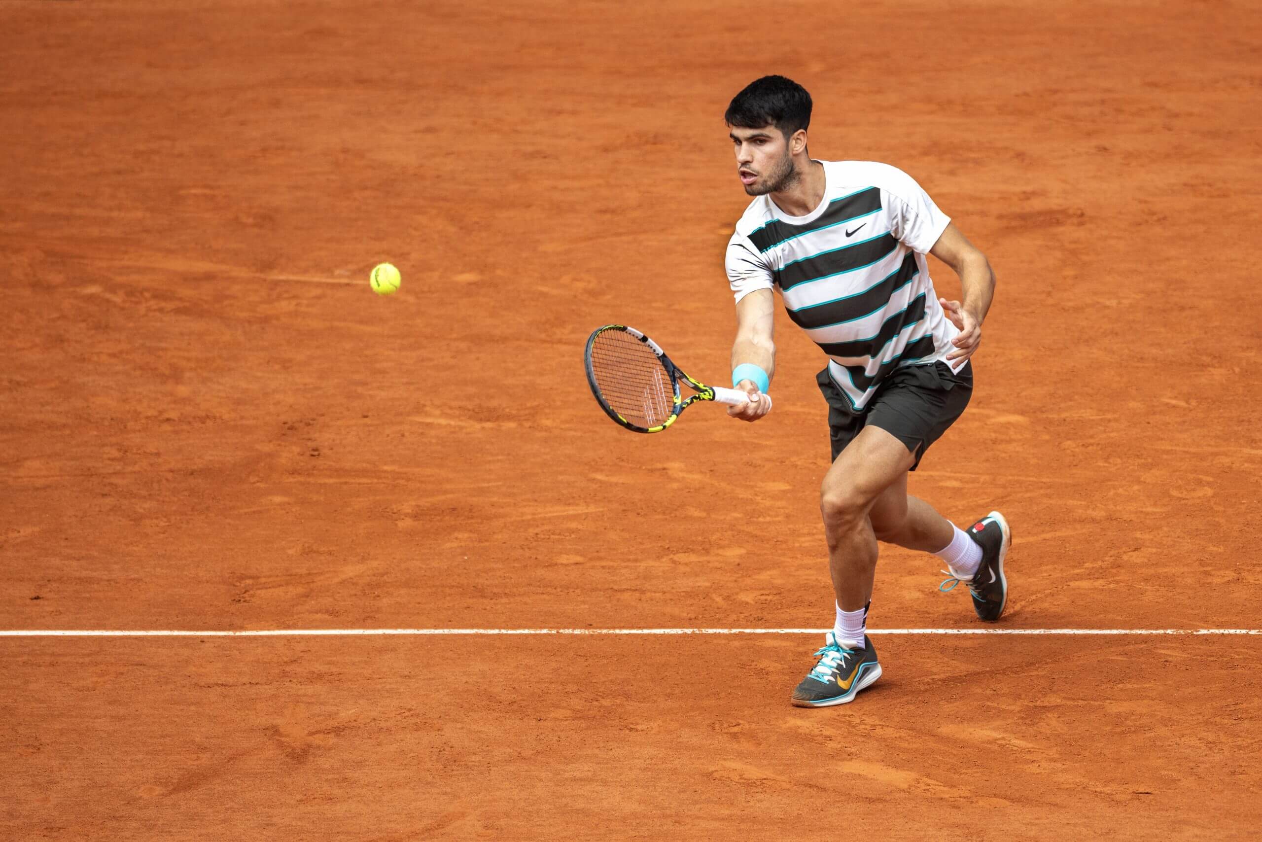 Carlos Alcaraz hits a drop shot on a clay court.