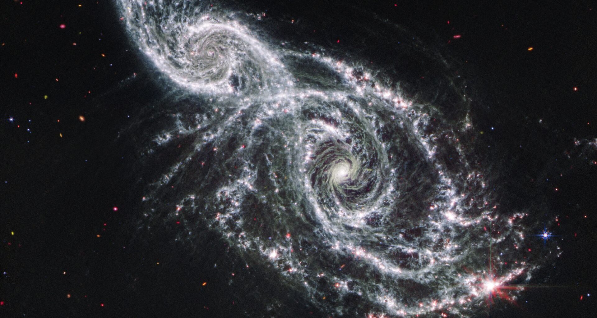 A deep space image showing the white gas and stars forming two spiral galaxies next to each other, stretching from the bottom right to top left of the image.