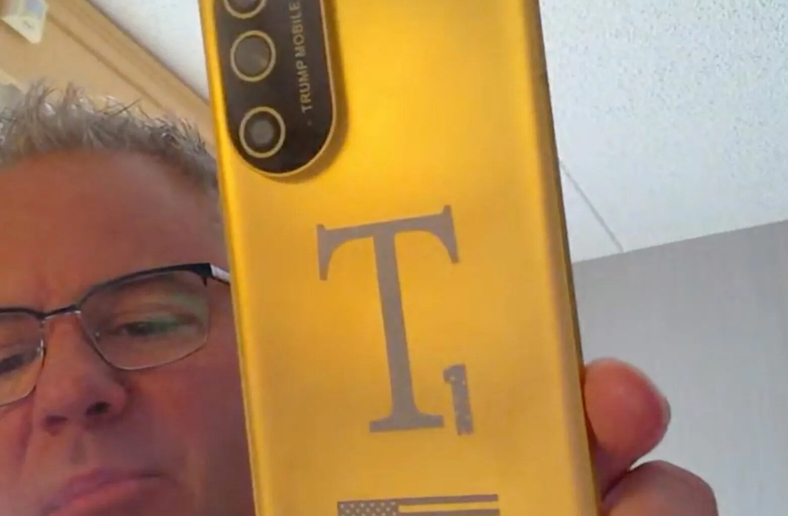 A person holding a gold Trump Mobile phone with a large 'T1' logo and an American flag on its back.