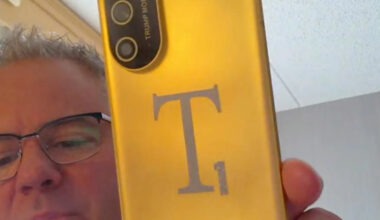 A person holding a gold Trump Mobile phone with a large 'T1' logo and an American flag on its back.