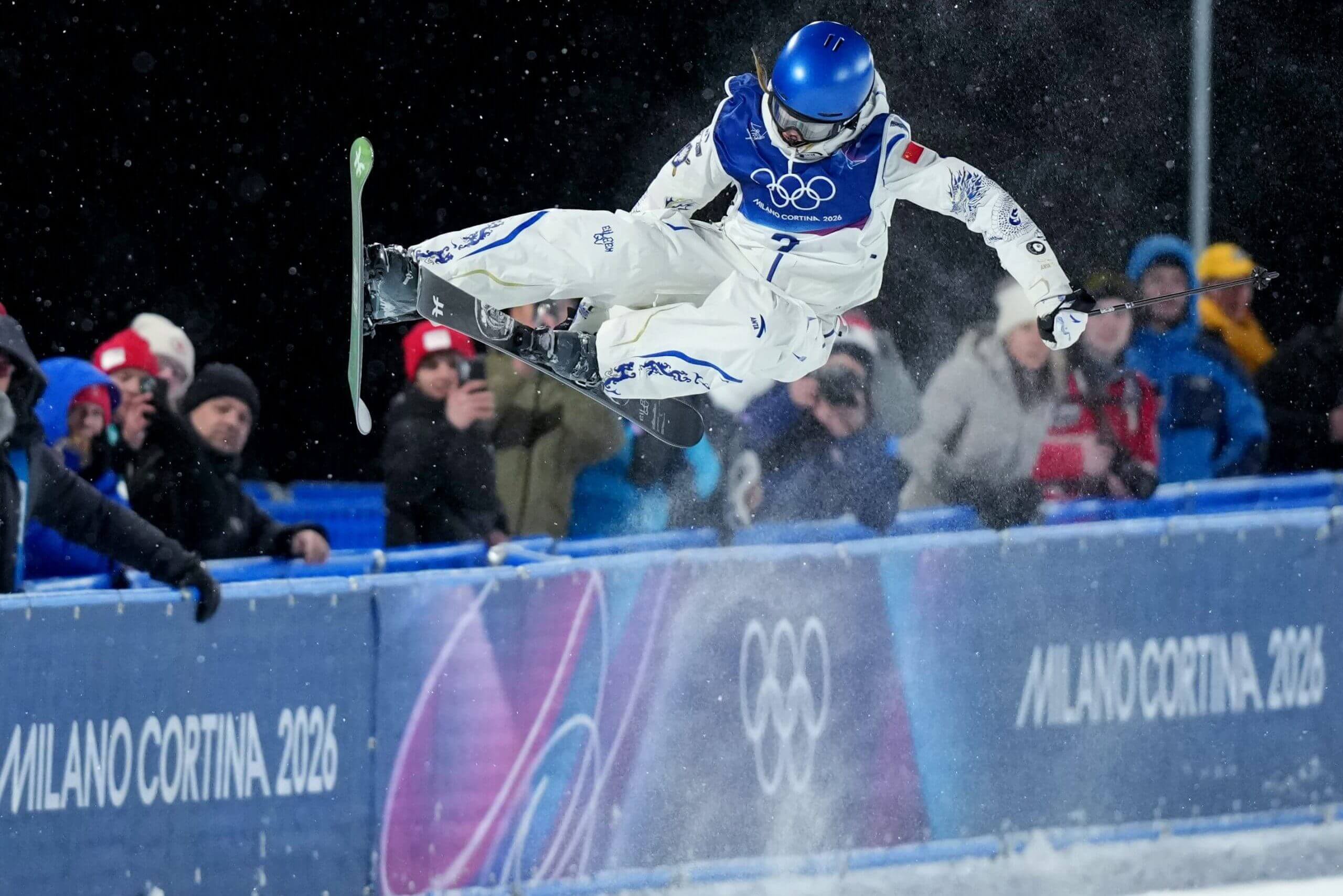 Eileen Gu, with a blue helmet and a white ski suit, rises during a move in the halfpipe qualifying at the 2026 Olympics on Feb. 19, 2026.