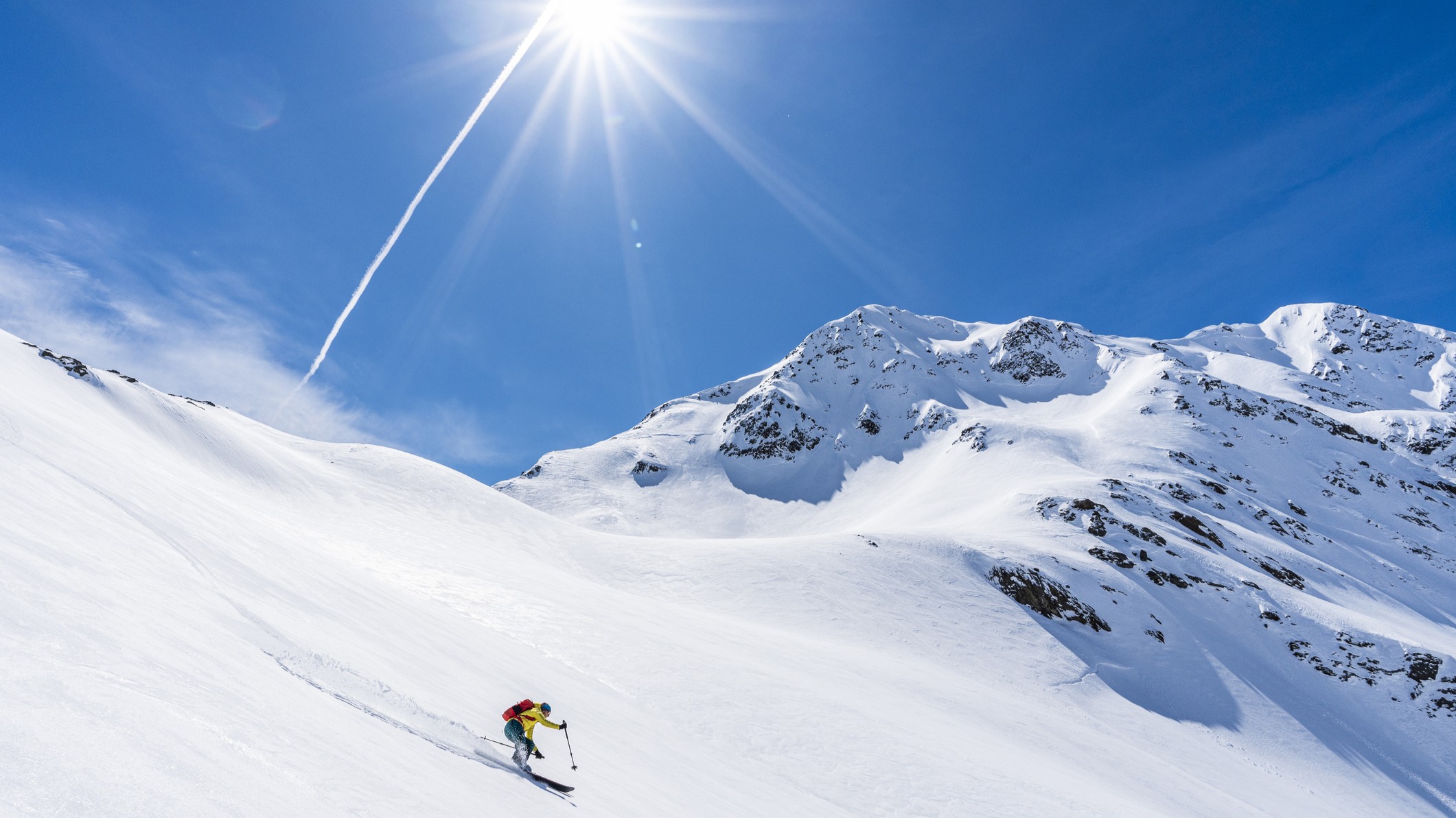 a person skies off piste on a beautiful sunny day with blue skie and snowy mountains in the background.