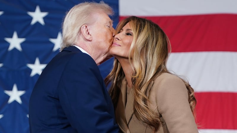 President Donald Trump kisses the First Lady Melania Trump on the cheek in from of a giant USA flag