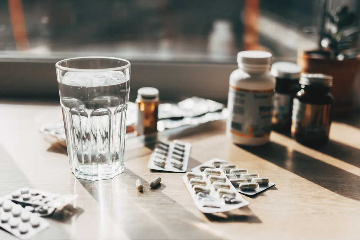 A variety of pills and jars on a surface, with a glass of water