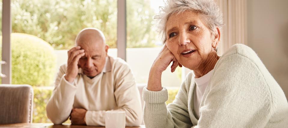 Retired couple sitting at kitchen table, mid-discussion.