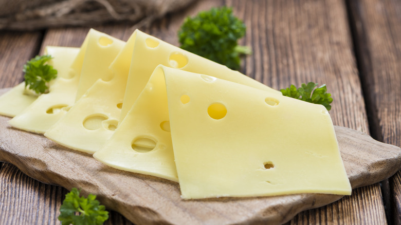 slices of swiss cheese on wooden cutting board with green garnish