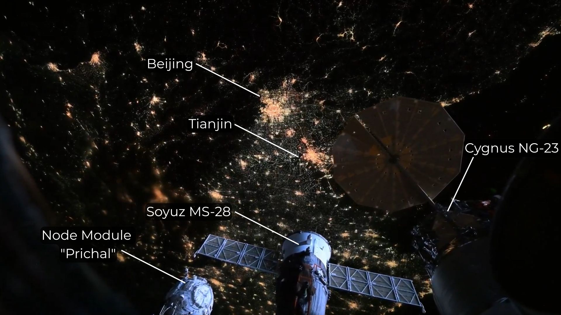 City lights are visible on the night side of Earth between the solar panels of docked spacecraft in a picture captured from the International Space Station.