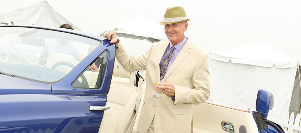 Wealthy man standing beside a Rolls Royce at a polo club.