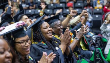 Graduates in caps and gowns smile and clap during Cal State LA’s Black Graduation ceremony, with cheering guests in the background.