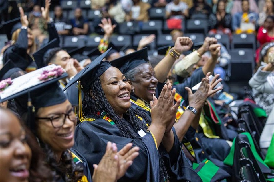 Graduates in caps and gowns smile and clap during Cal State LA’s Black Graduation ceremony, with cheering guests in the background.