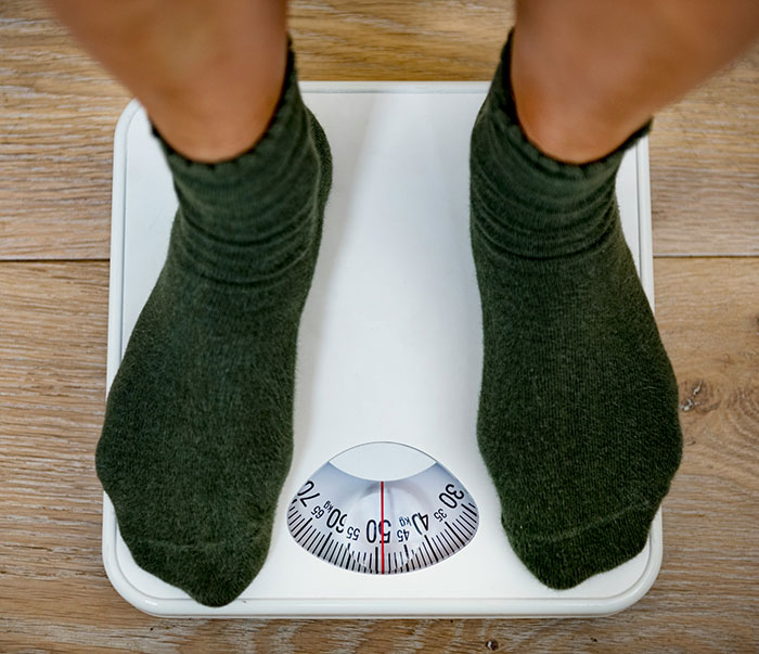 Person wearing dark socks standing on a scale showing a weight around 50, a weirdly hilarious image for your feed.