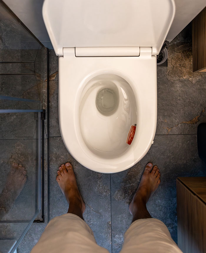 Top-down view of a person standing barefoot in front of a toilet with an object inside, a weirdly hilarious image.
