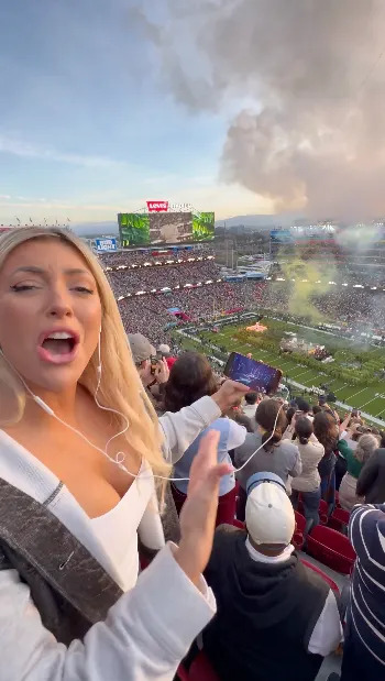 Fan in sports apparel excitedly reacts during a stadium event with fireworks; crowd and field visible in the background