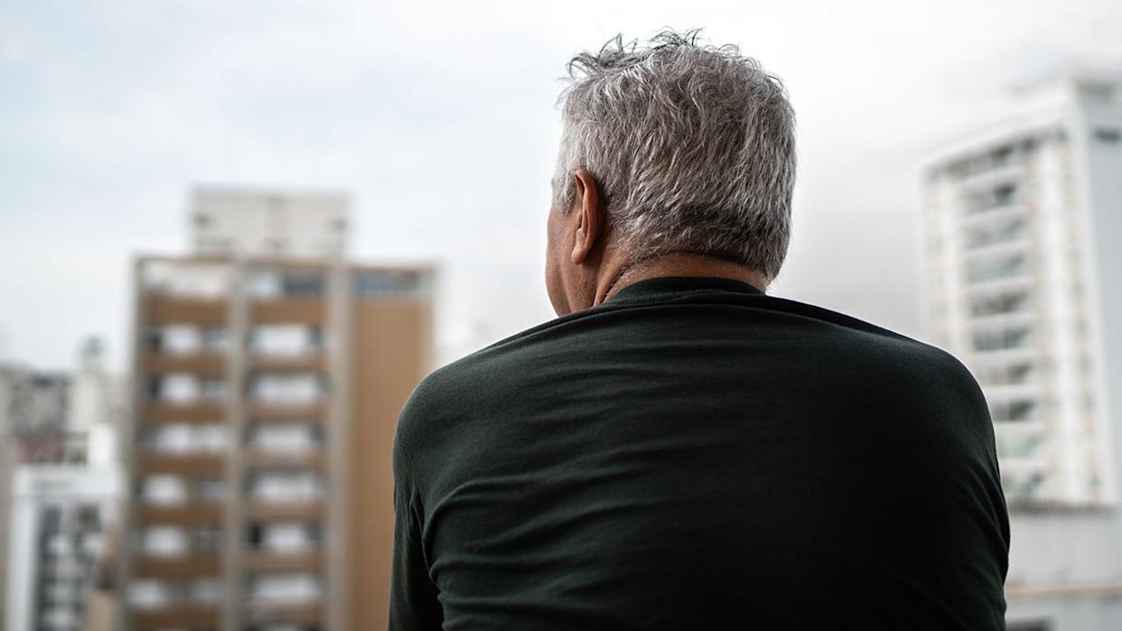 senior man sitting outside overlooking city buildings