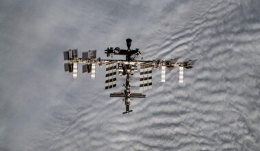 long-distance shot of the international space station from above, with cloudy earth skies in the background
