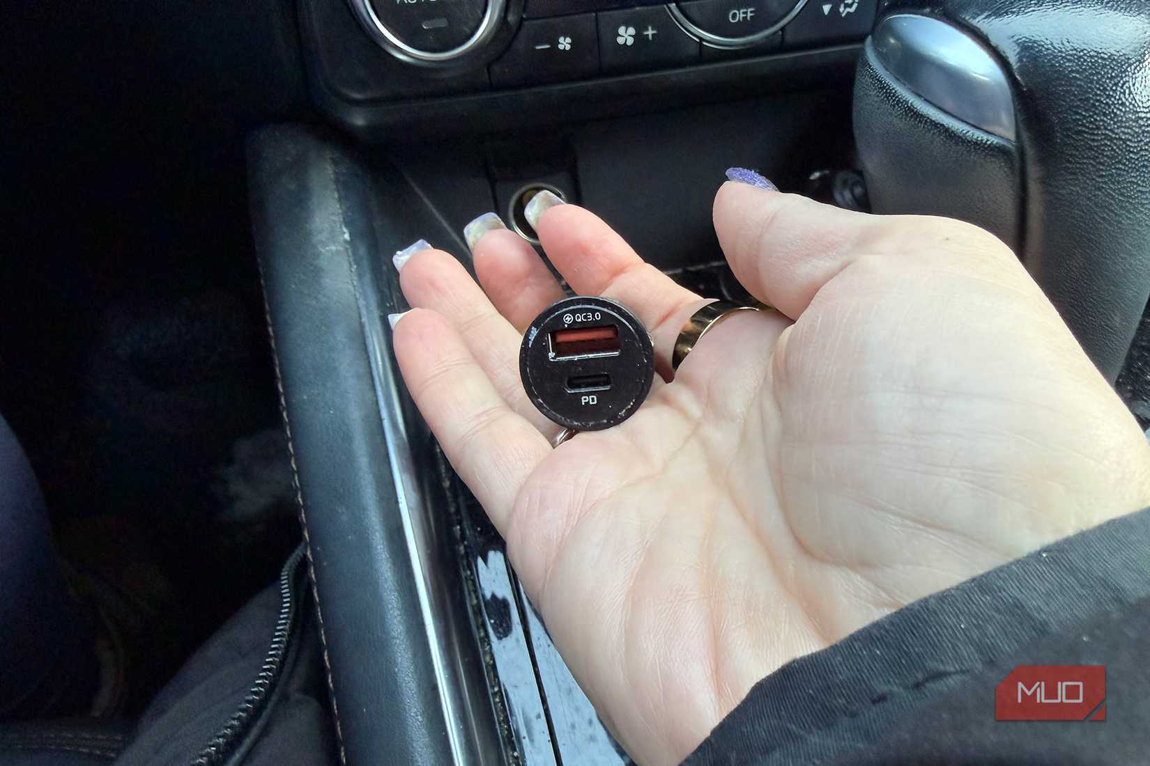 A hand holding a car charger in a vehicle.