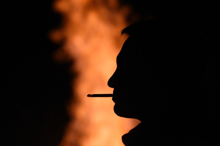 A close-up of a silhouette of a man smoking a cigarette in front of a bonfire