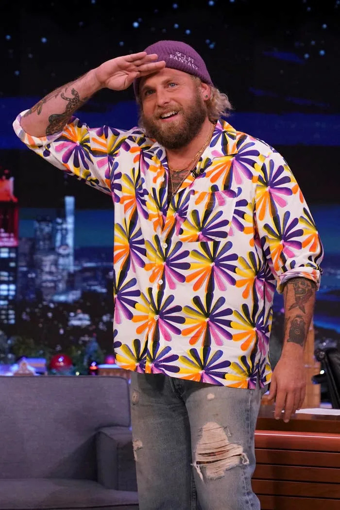 Person in floral shirt and jeans salutes on a talk show set