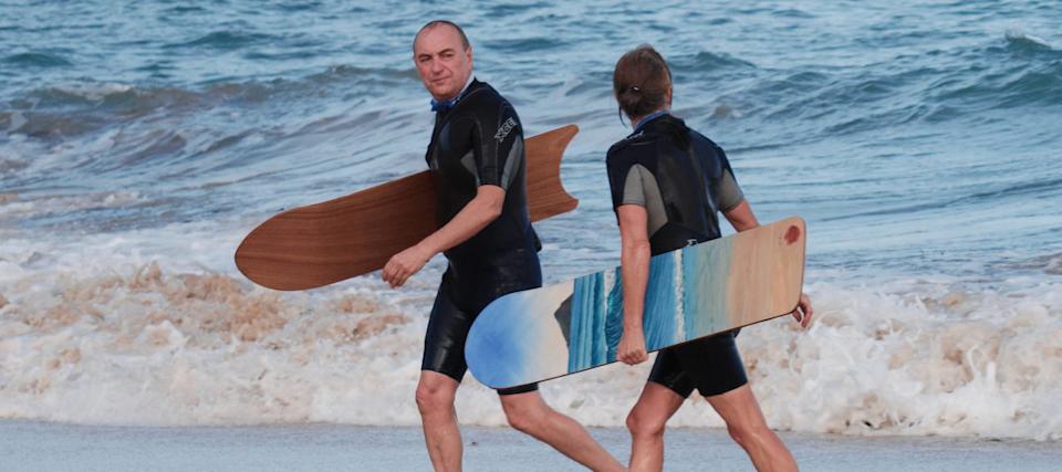 Two surfers walk along the beach on a cloudy day.