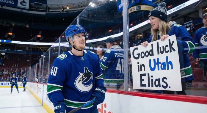 Vancouver Canucks center Elias Pettersson smiles as he looks up at a female fan pressing a handmade sign against the rink glass that reads "Good luck in Utah Elias." during pre-game warmups.