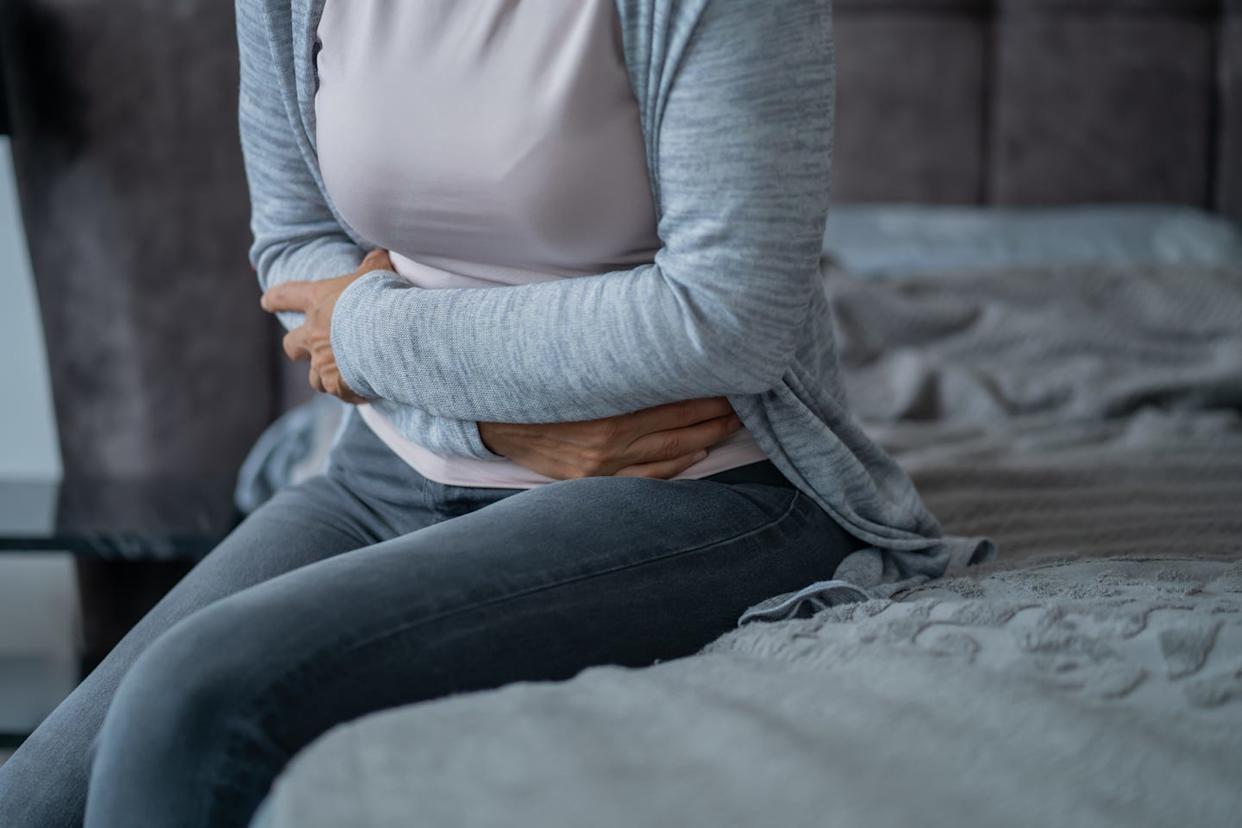 woman experiencing abdominal pain holding stomach while sitting