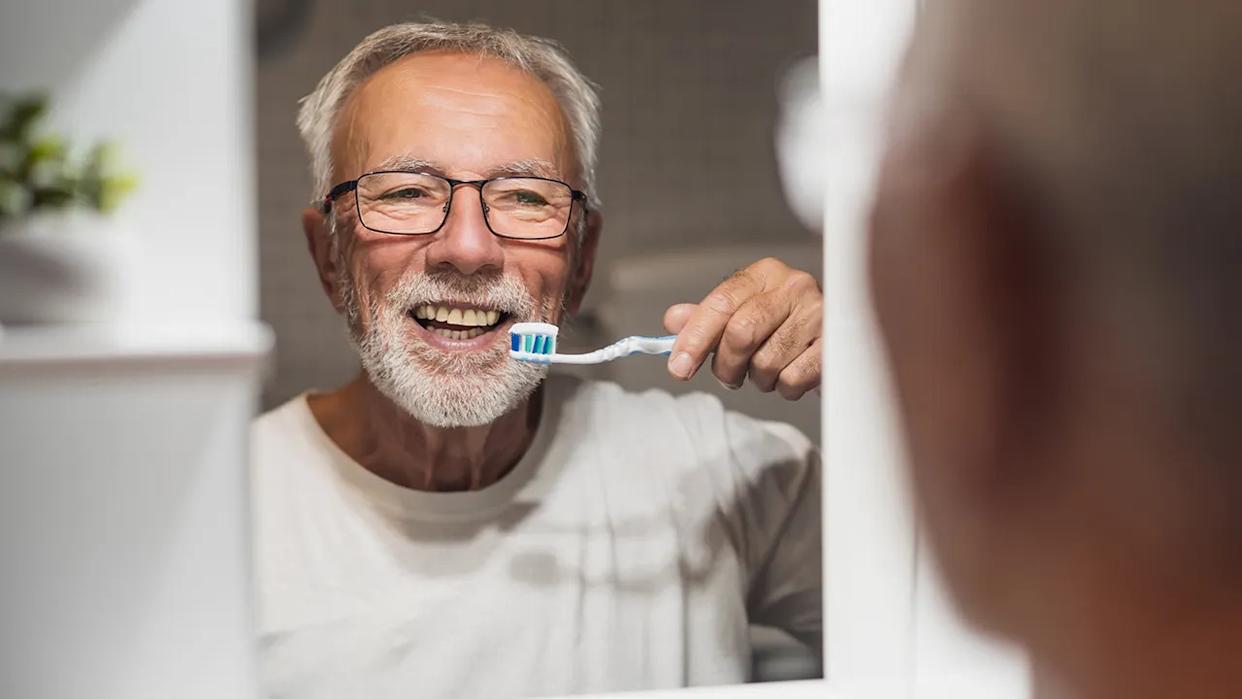 senior man smiles into mirror before brushing teeth