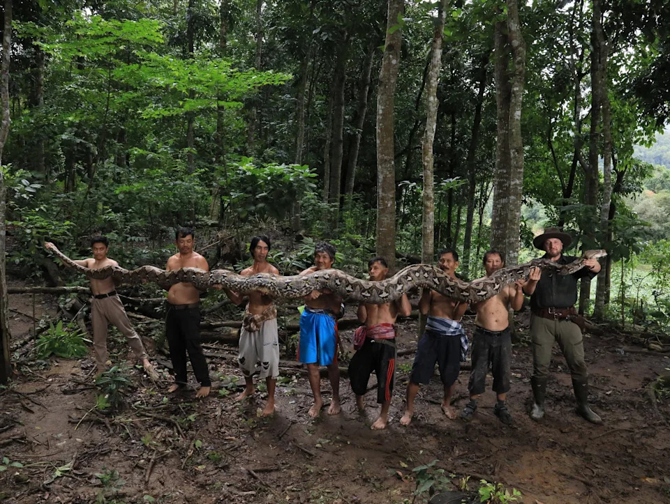 A group of men stand in a line holding the long body of a snake.