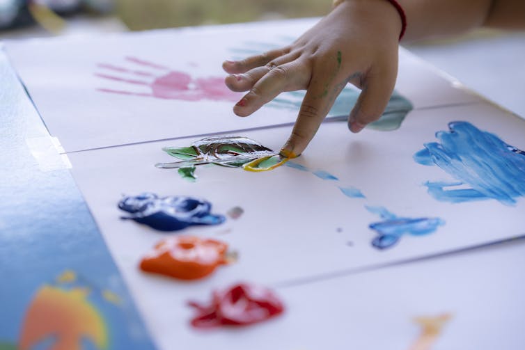 Close-up of child's hand fingerpainting on sheets of paper