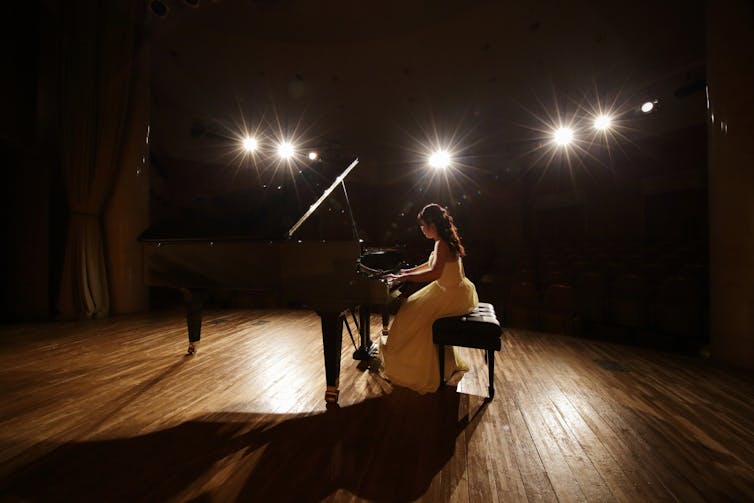 Young person playing piano on a spotlit stage