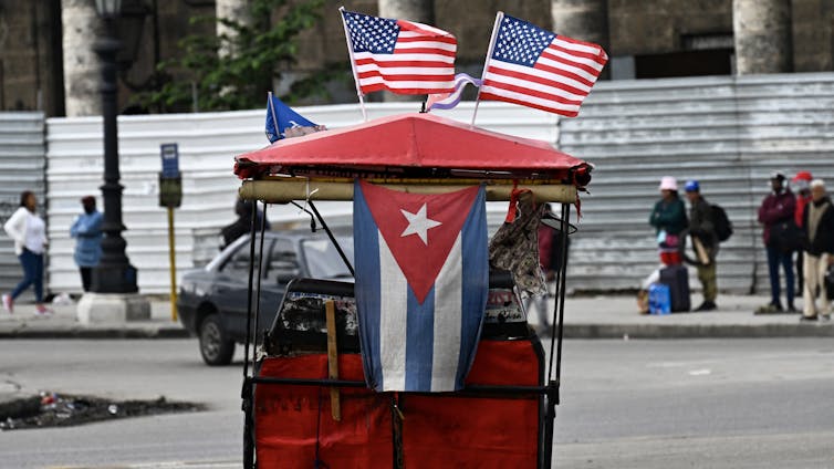 A tricycle has US and Cuban flags attached to it.