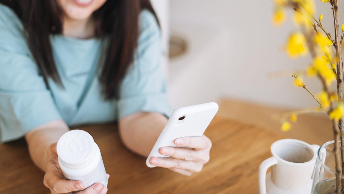 woman holding white prescription bottle in right hand and smartphone on the left hand