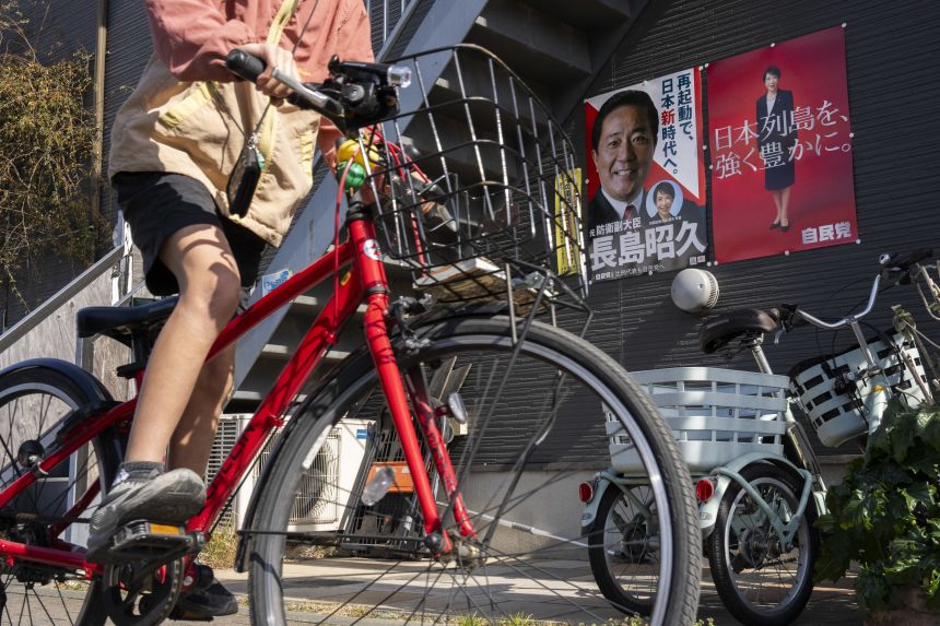 A child cycles past posters of Japan's Prime Minister Sanae Takaichi and a candidate running for the upcoming the House of Representatives election, in Inagi, Tokyo, on February 6, 2026.