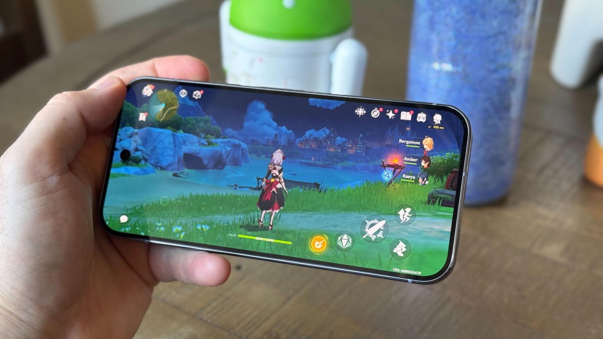 A smartphone playing an adventure game, Genshin Impact, in front of a table background.