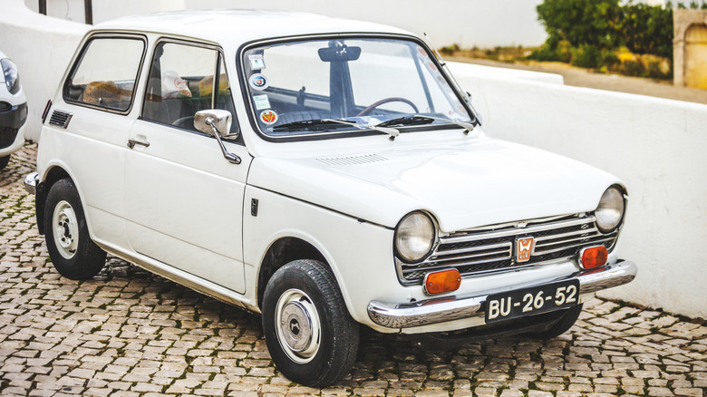A white Honda N600 parked on cobblestone
