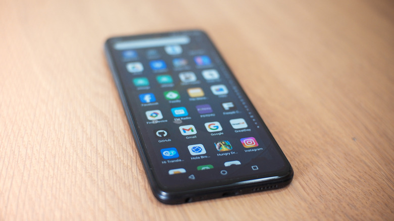 Android smartphone lying on a wooden surface with app icons visible on the screen.