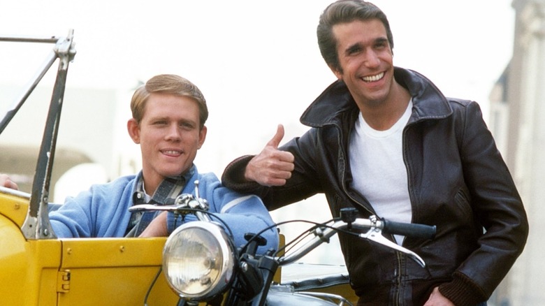 Smiling Richie sits in hotrod beside the Fonz on his motorcycle
