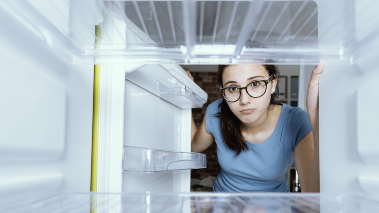 A close-up image of woman looking into empty fridge with a sad look on her face