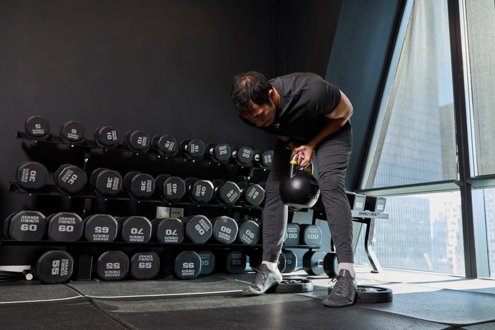 individual lifting a kettlebell in a gym setting with dumbbells in the background individual lifting a kettlebell in a gym setting with dumbbells in the background