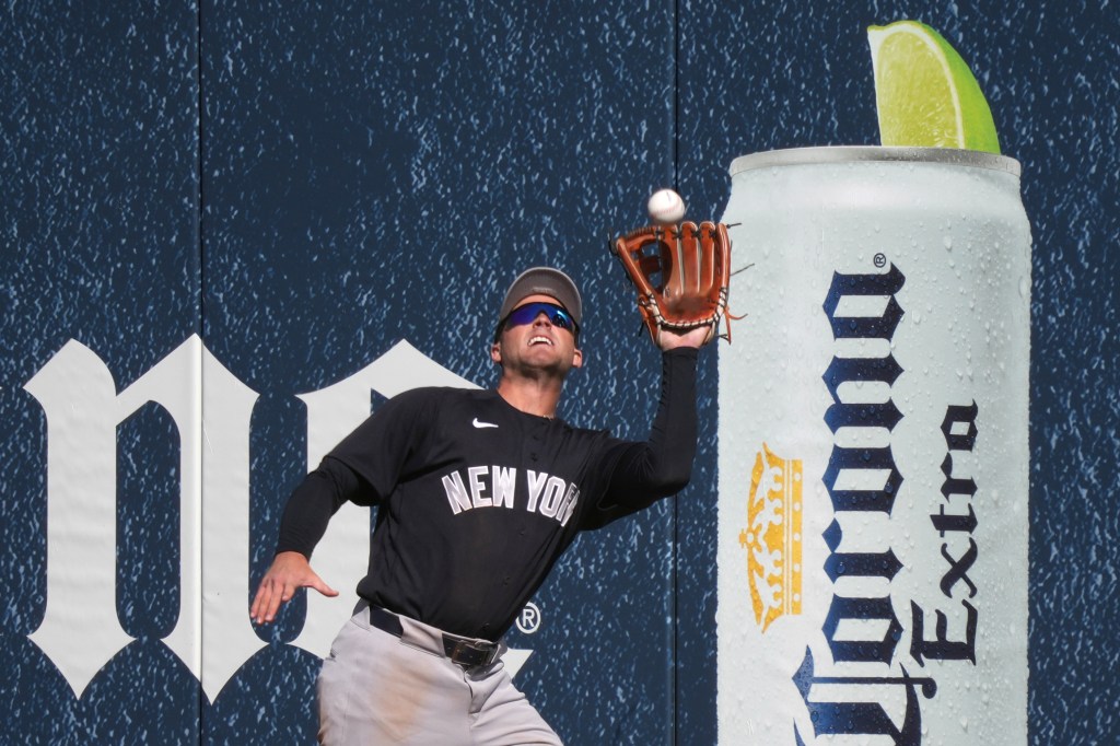 Max Schuemann of the New York Yankees catches a fly ball next to a large advertisement for Corona Extra beer.