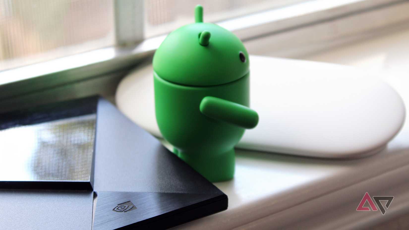 An Android bot figurine with its back turned to the Nvidia Shield TV, looking towards a Google TV Streamer.