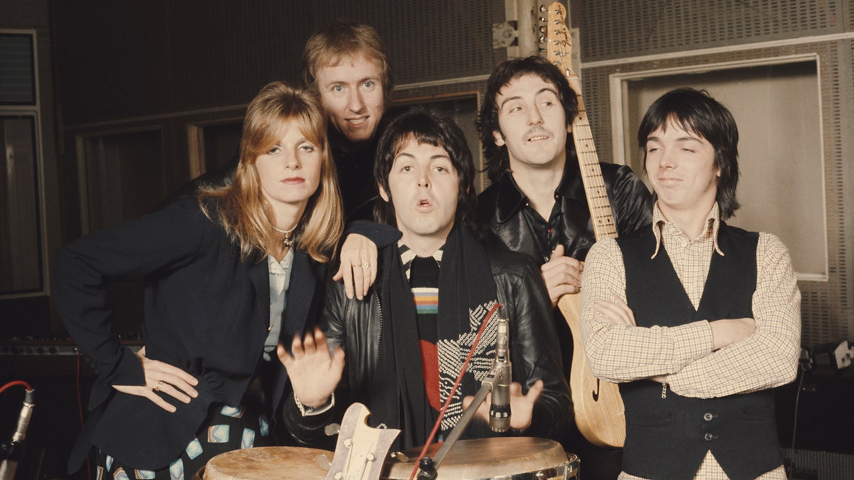 Linda McCartney, Geoff Britton, Paul McCartney, Denny Laine, and Jimmy McCulloch standing together in a recording studio.