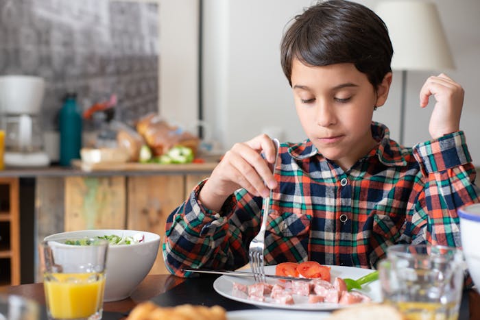 Young boy eating breakfast alone at kitchen table, illustrating parenting and family conflict themes. Young boy eating breakfast alone at kitchen table, illustrating parenting and family conflict themes.