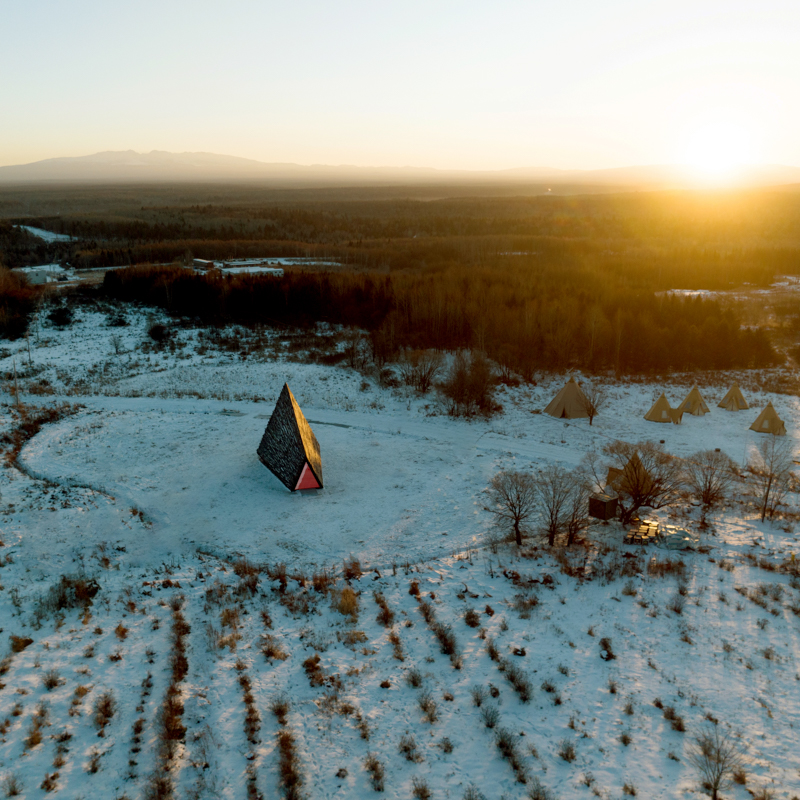 reflective red chamber emerges from prism mountain shelter’s charred wood shell