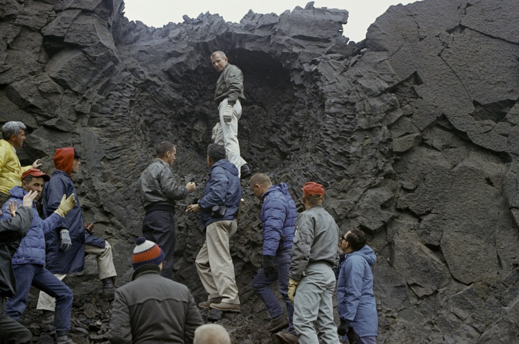 Apollo astronauts stand next to a grey cliff in Iceland.