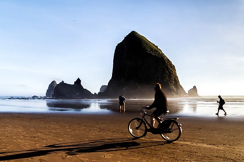 People enjoying a serene morning on the beach at Cannon Beach with the Haystack Rock in the background.