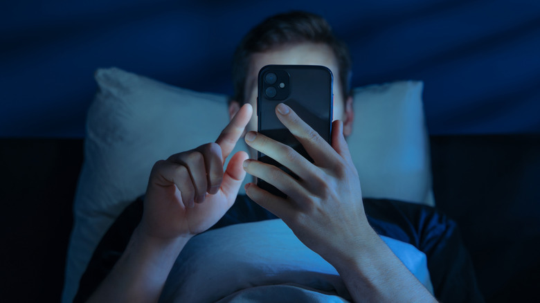 Man holding a phone in bed in a dark room