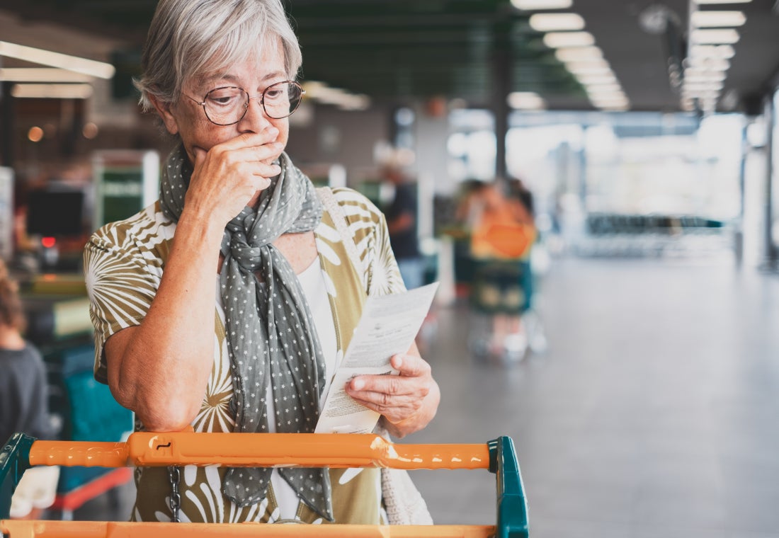 A person grocery shopping, looking down at their list and appearing concerned.